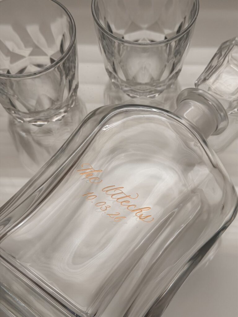 Engraved glass decanter and two crystal whiskey glasses on a white background