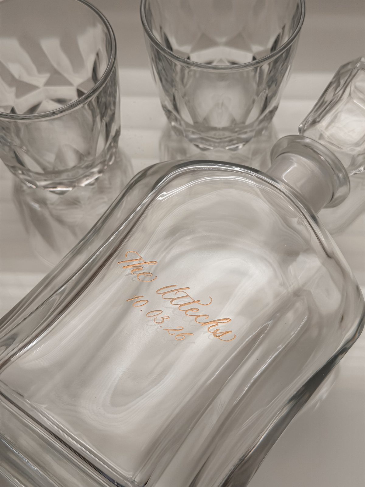 Engraved glass decanter and two crystal whiskey glasses on a white background