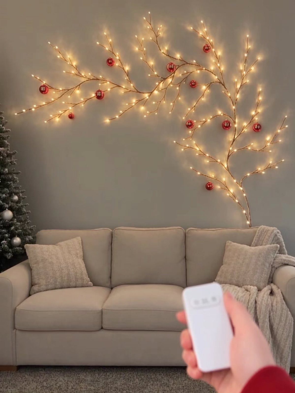 Branch-shaped wall lights with red ornaments above a beige sofa in a living room