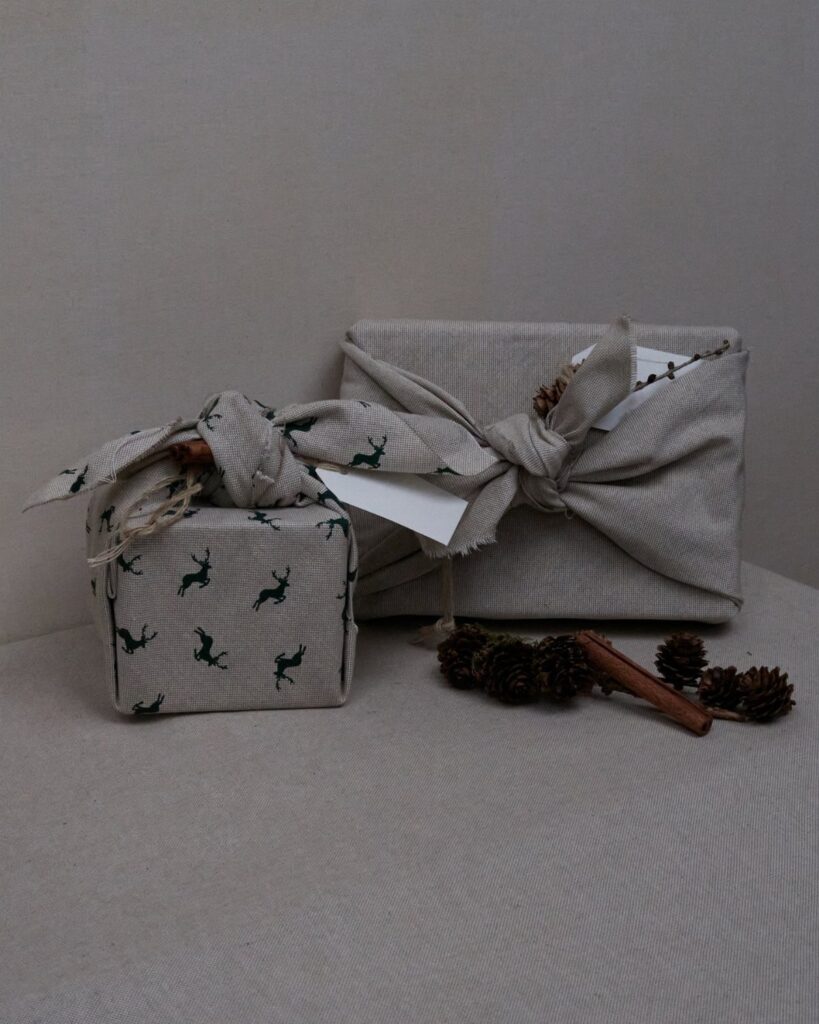 Fabric wrapped gifts with deer patterns, tied with bows and decorated with pinecones.