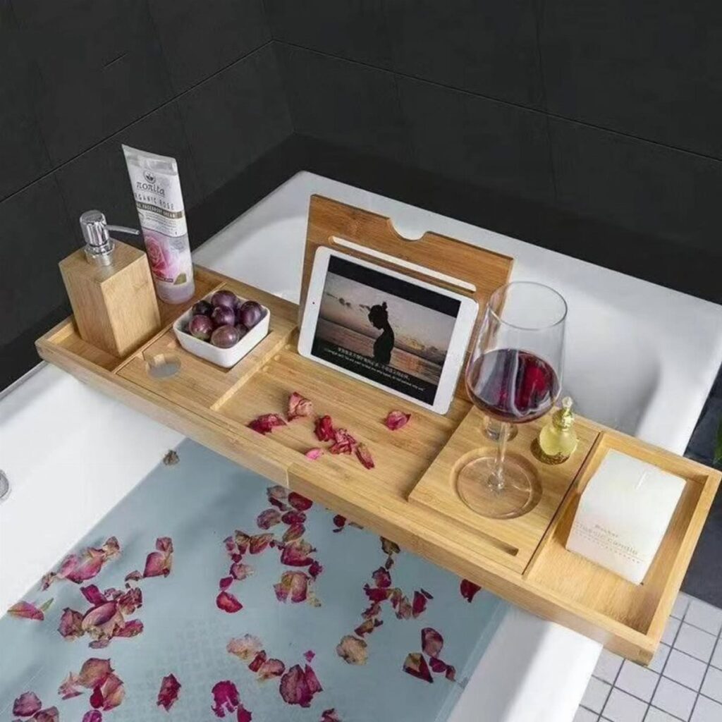 Bamboo bathtub caddy holding a tablet, wine, and grapes over a petal-filled bath