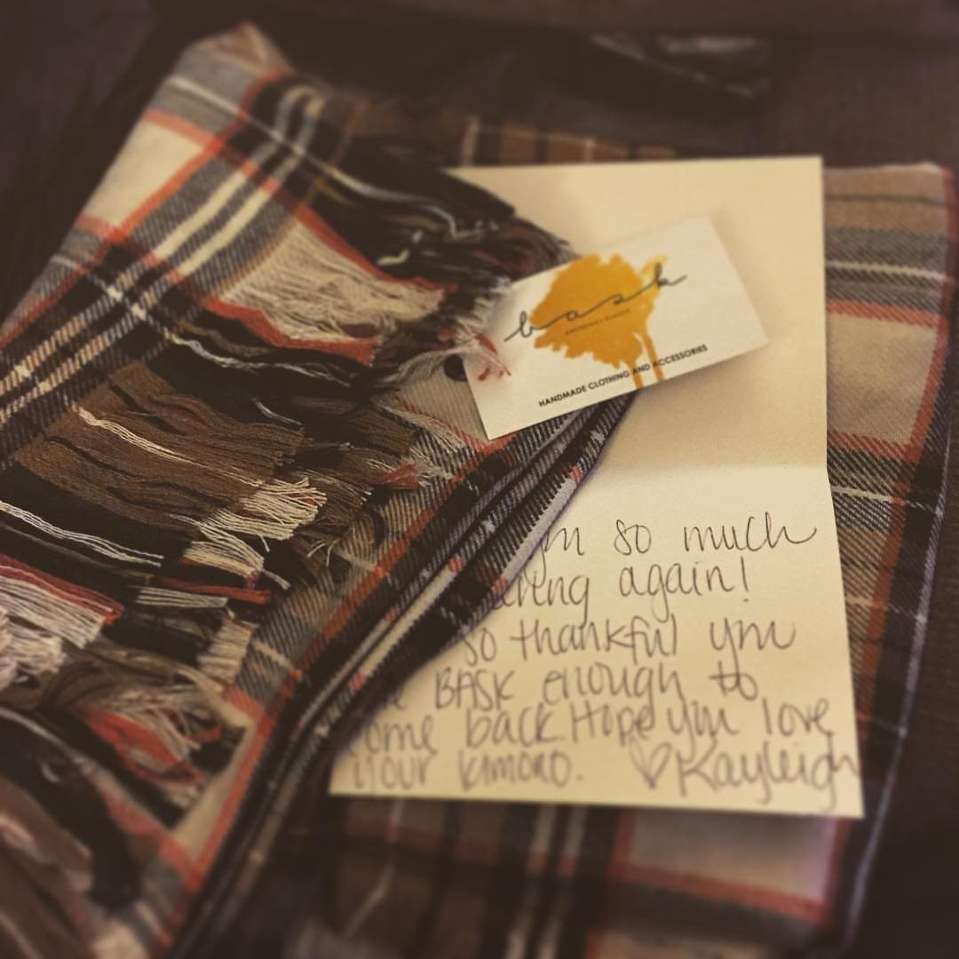 Handwritten thank you note resting on a plaid scarf with a small business card.