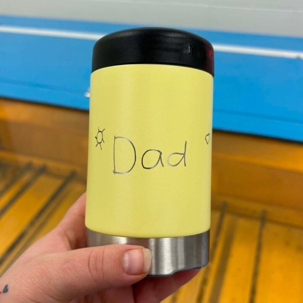 Yellow insulated travel mug with Dad handwritten on it held by a hand