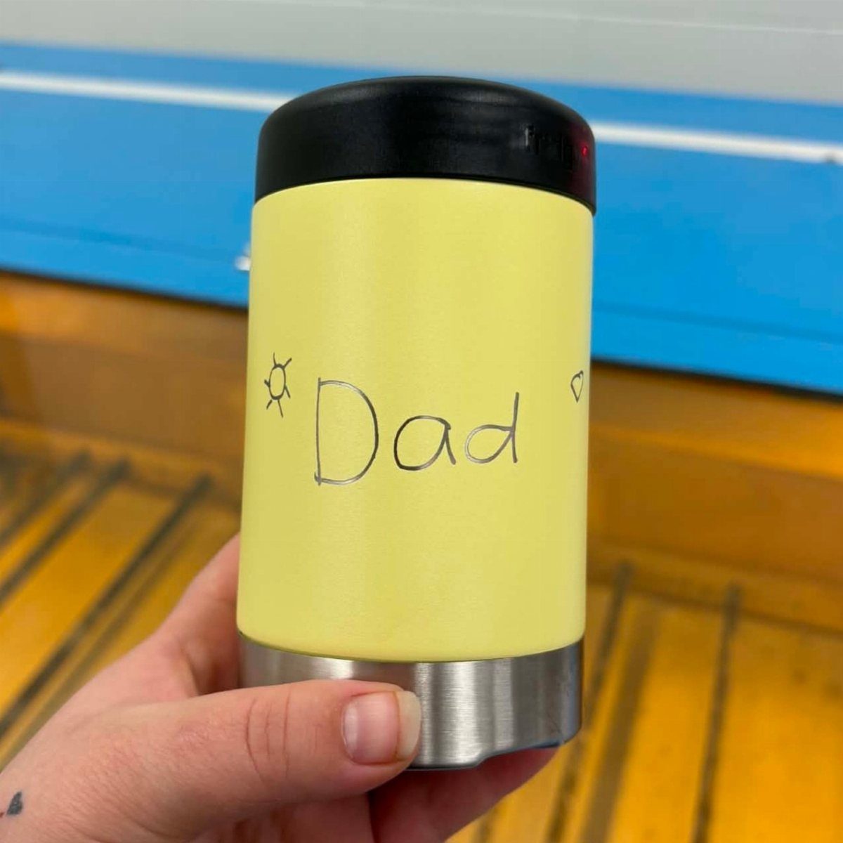 Yellow insulated travel mug with Dad handwritten on it held by a hand