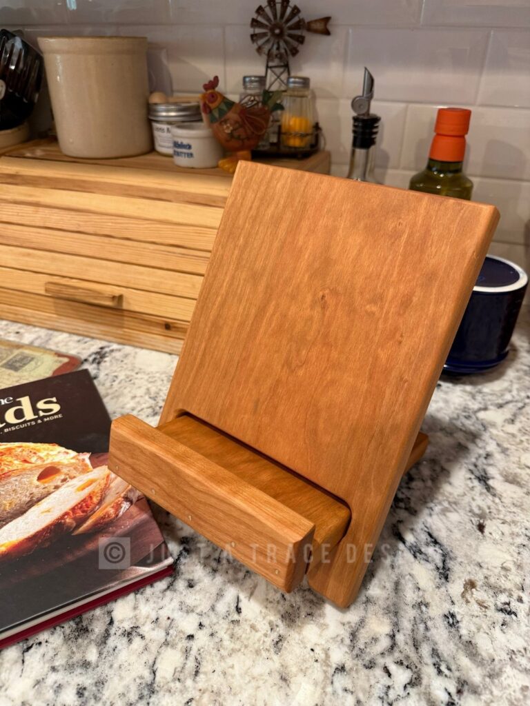 Wooden cookbook stand on a granite kitchen counter next to a cookbook.