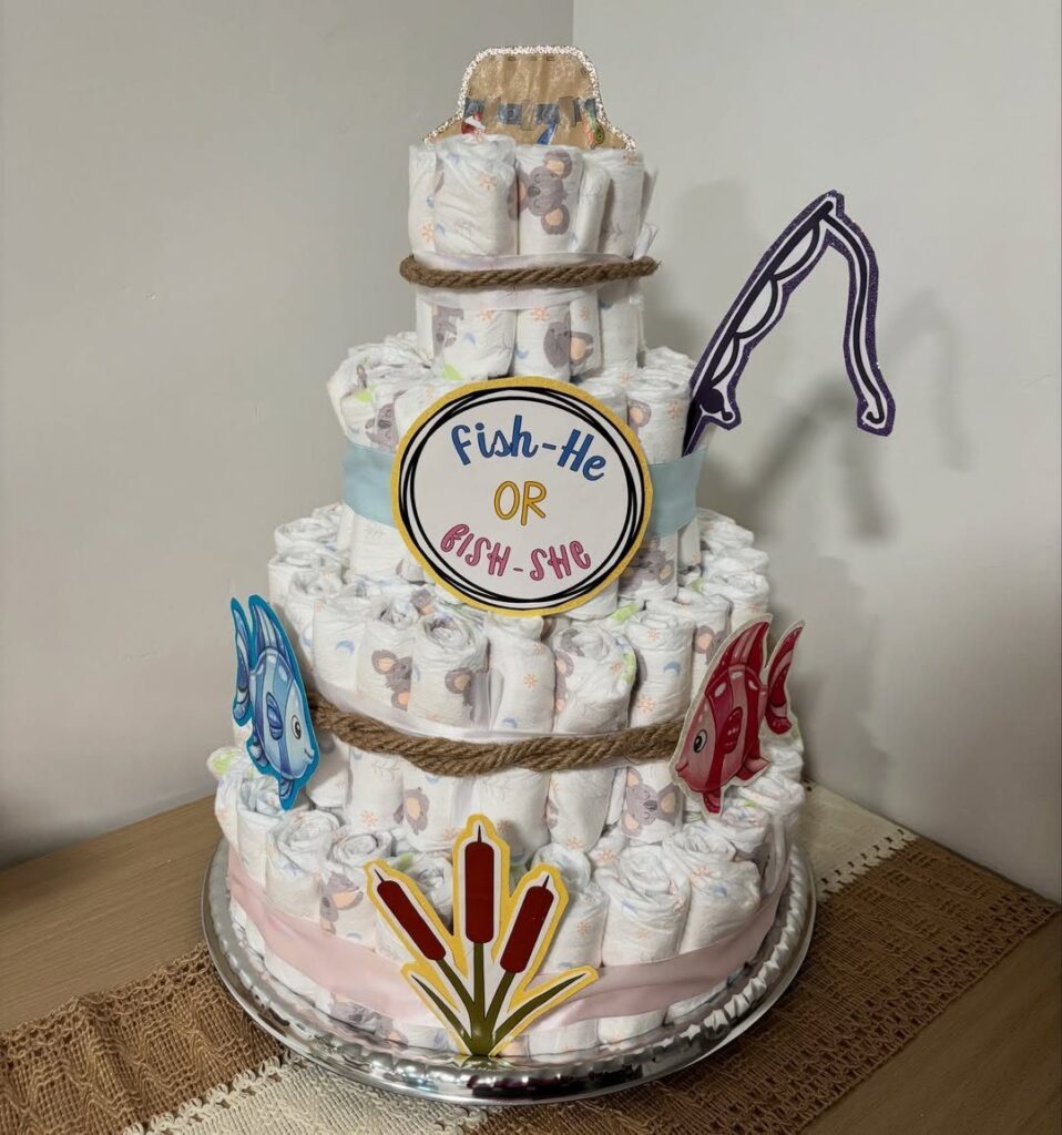 Three-tiered diaper cake decorated with fish cutouts and a gender reveal sign.