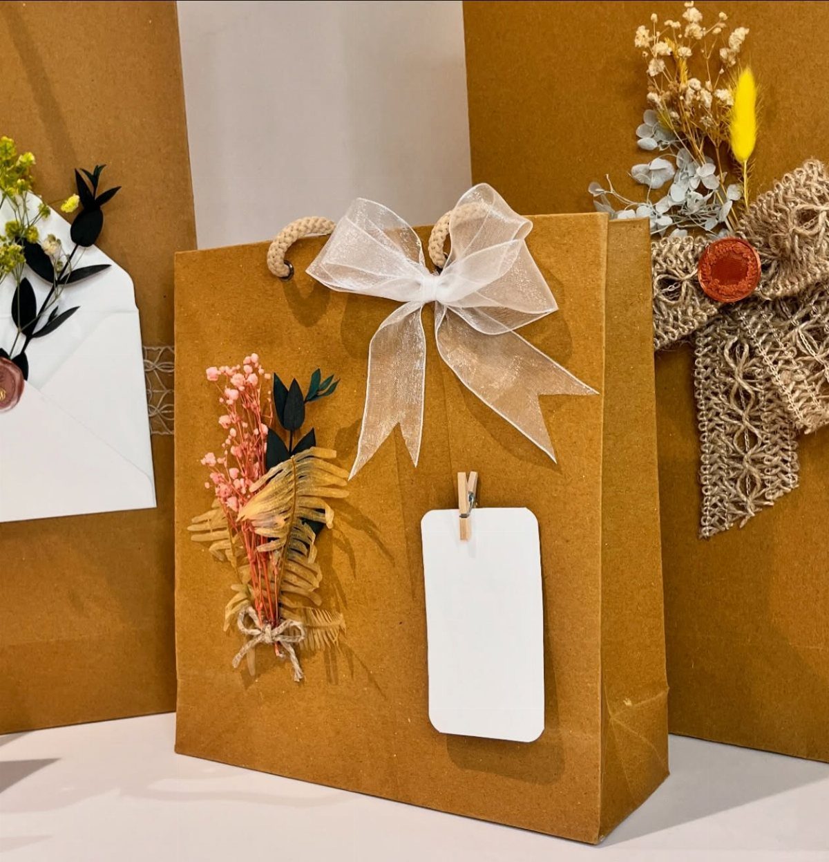 Brown paper gift bag decorated with a white bow and dried flowers.