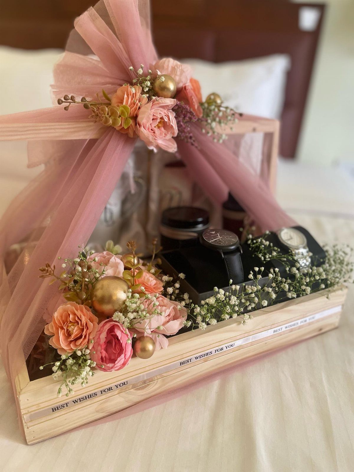 Wooden gift crate with two wristwatches, pink flowers, and a large tulle bow.