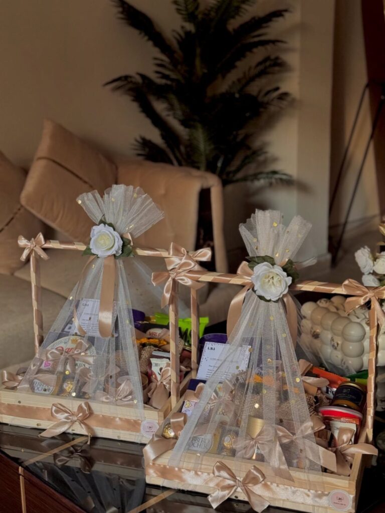 Two wooden gift baskets wrapped in white tulle with satin bows and roses.