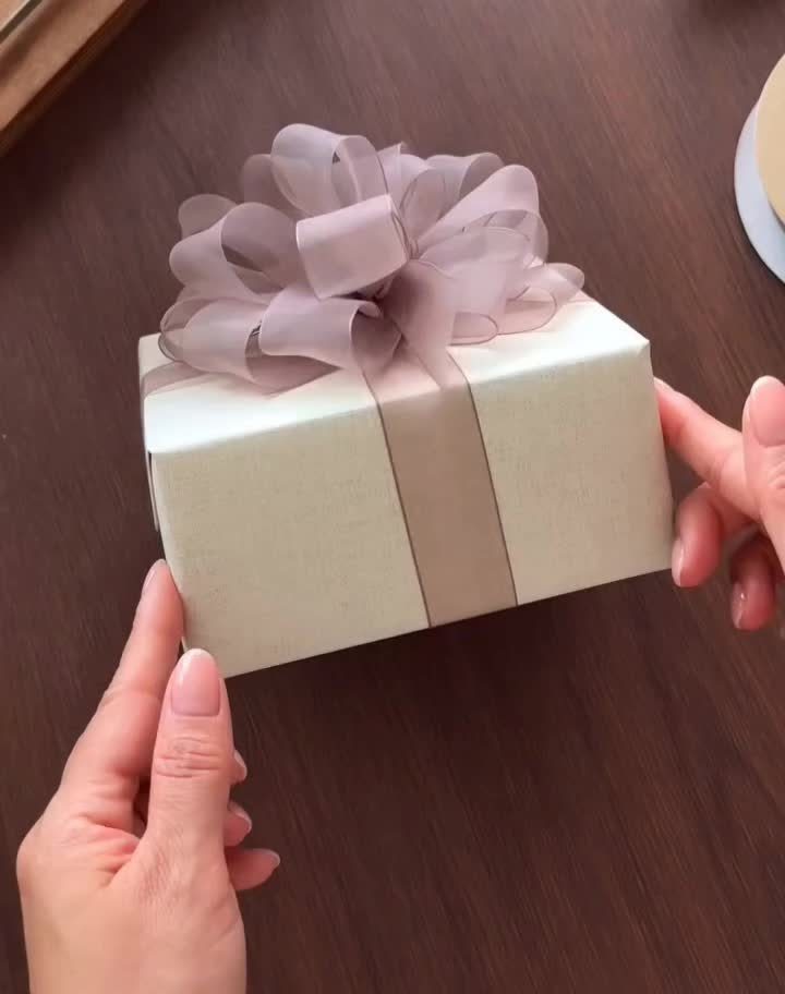White gift box with a large mauve sheer ribbon bow held by hands.