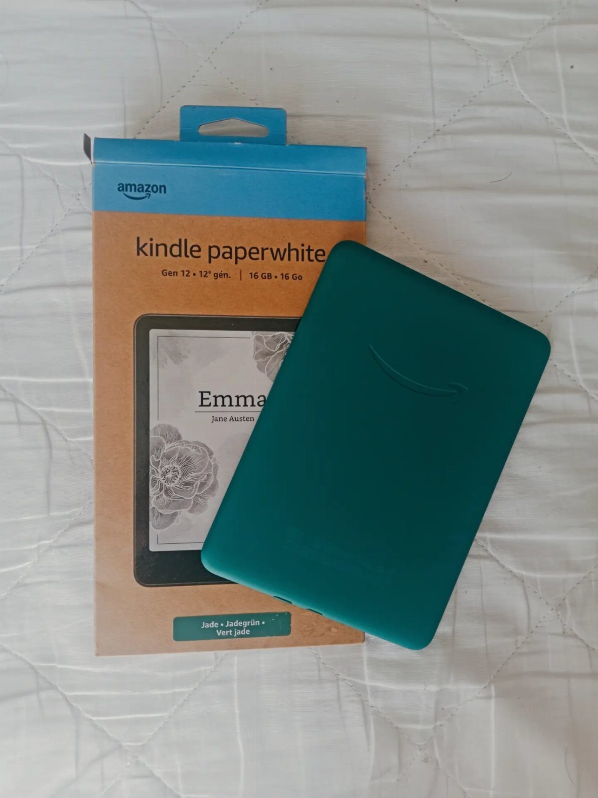 Teal Kindle Paperwhite e-reader with case resting on its original Amazon packaging.