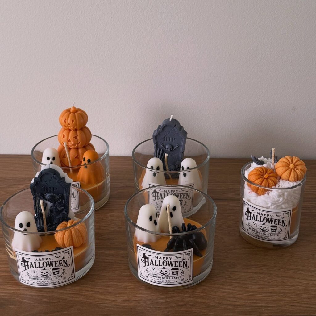 Halloween candles in glass jars with ghosts, pumpkins, and tombstones on wooden table