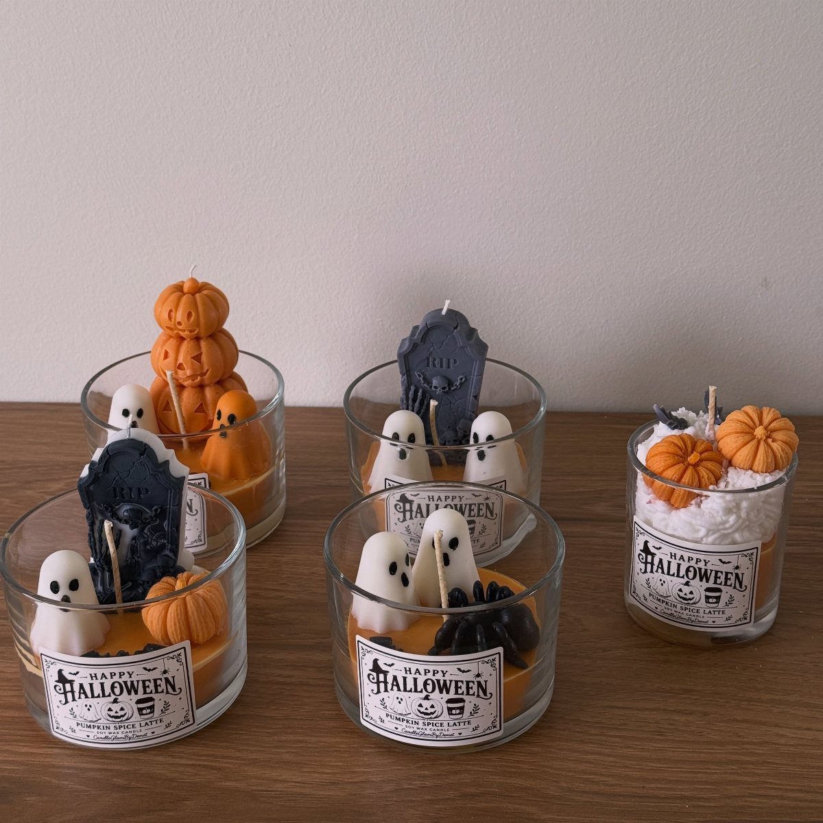 Halloween candles in glass jars with ghosts, pumpkins, and tombstones on wooden table