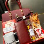 Gift box for grandma with burgundy handbag, wallet, white mug, and cookies.
