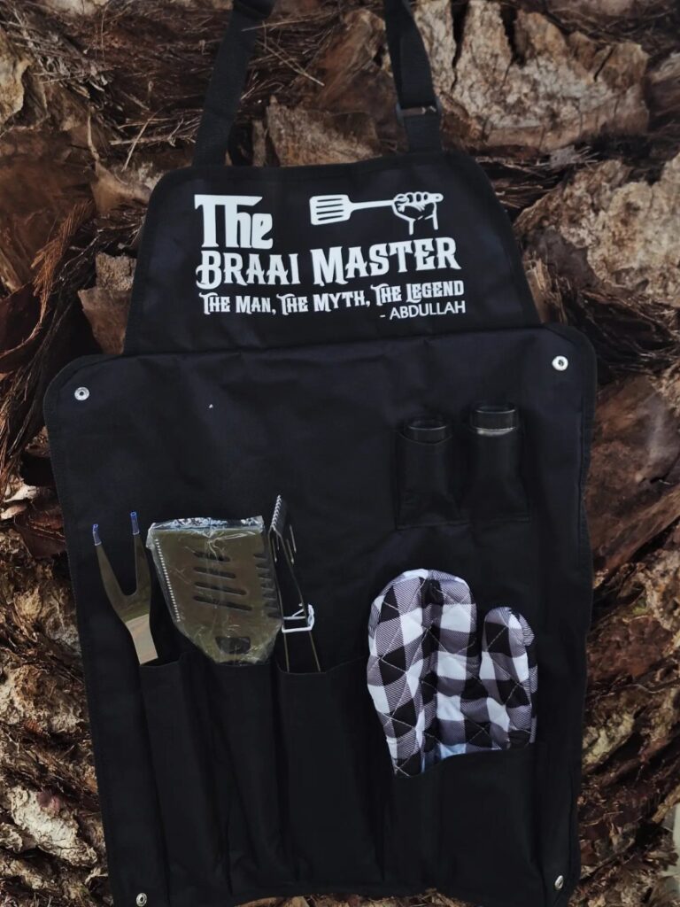 Black grilling apron with Braai Master text and tools on a wooden background