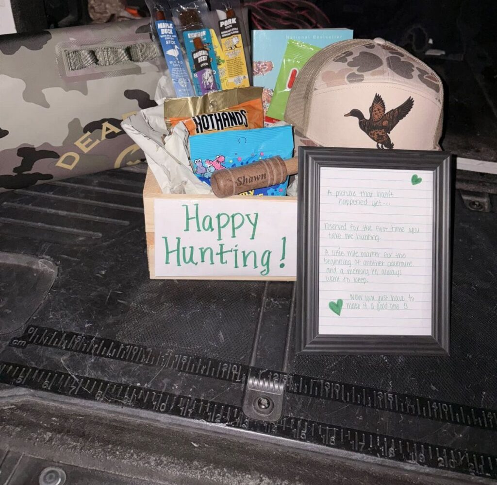Hunting gift basket in a wooden crate with snacks, camo hat, and note.