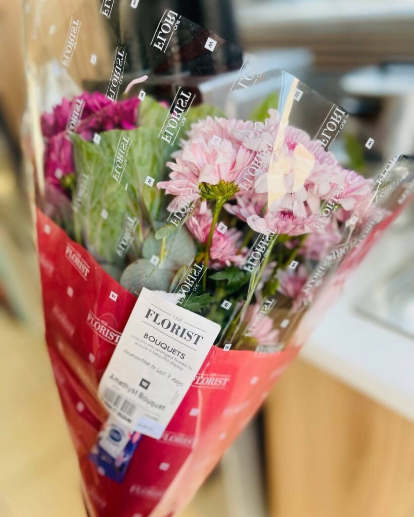 Bouquet of pink and purple flowers wrapped in red paper and clear plastic.