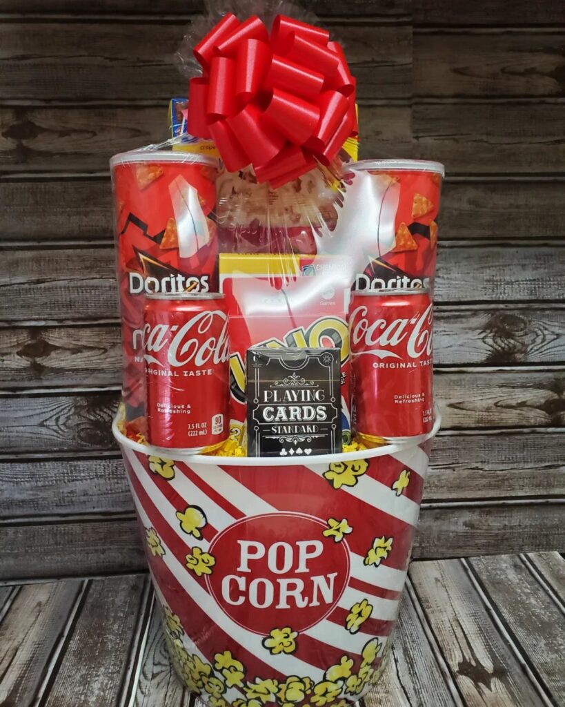 Movie night gift basket in a popcorn bucket with snacks and drinks.