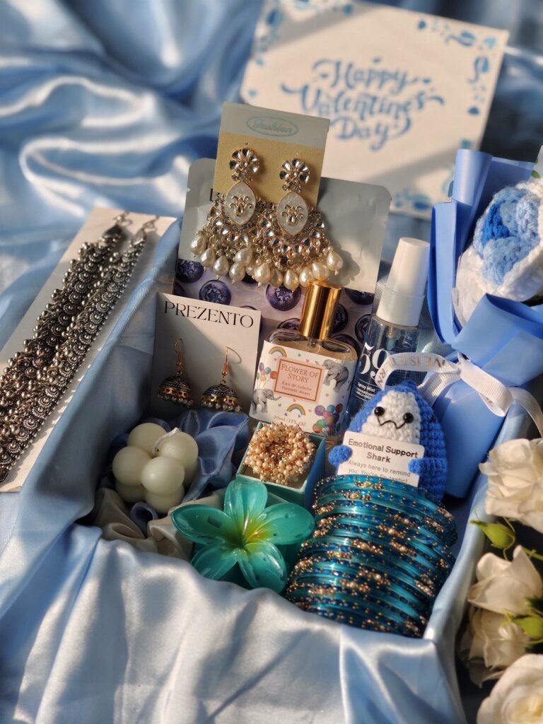 Gift box with blue satin lining containing jewelry, perfume, and a crochet shark.