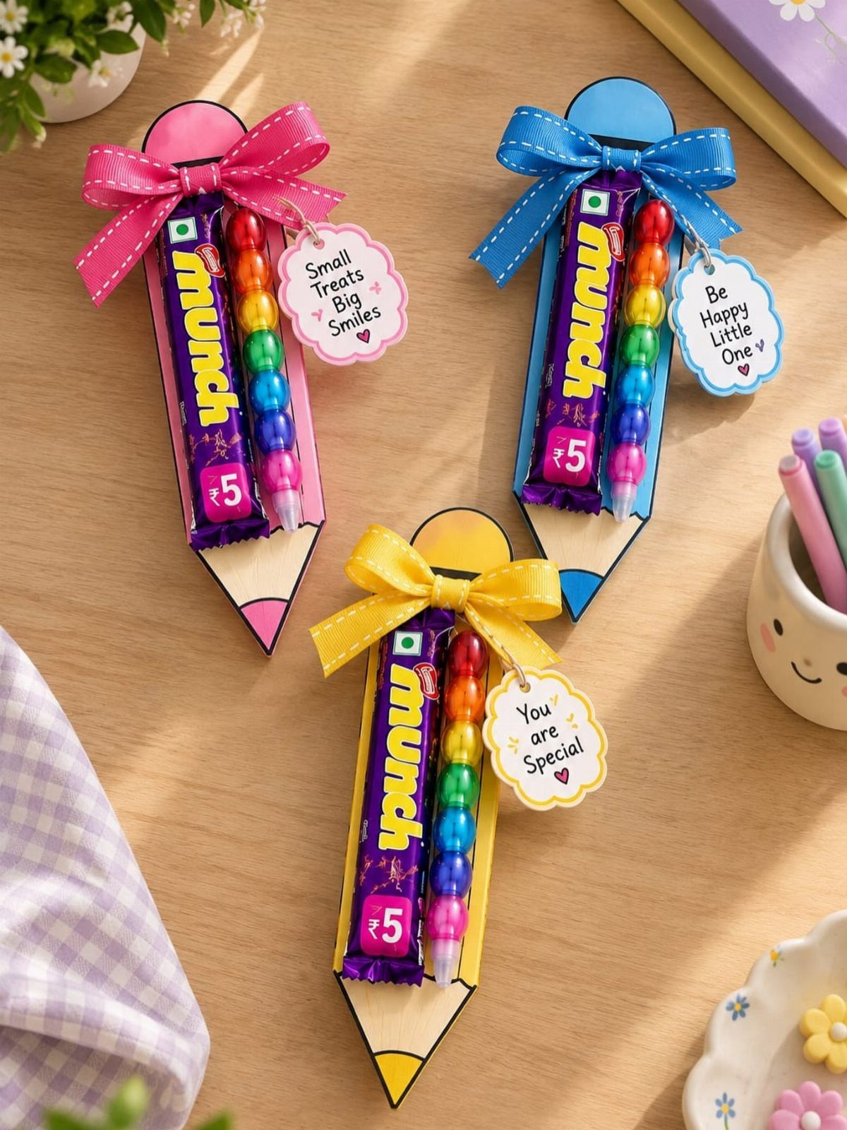 Pencil-shaped gift holders containing chocolate bars and colorful markers with decorative ribbons.