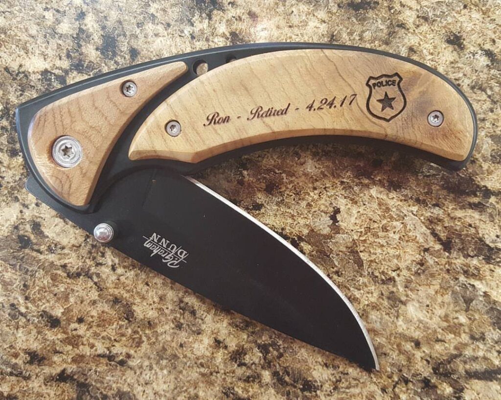 Engraved pocket knife with wooden handle and black blade on granite countertop