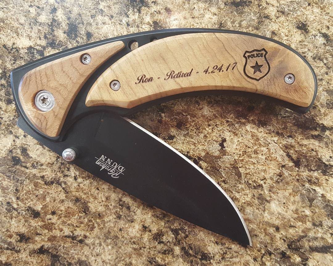 Engraved pocket knife with wooden handle and black blade on granite countertop