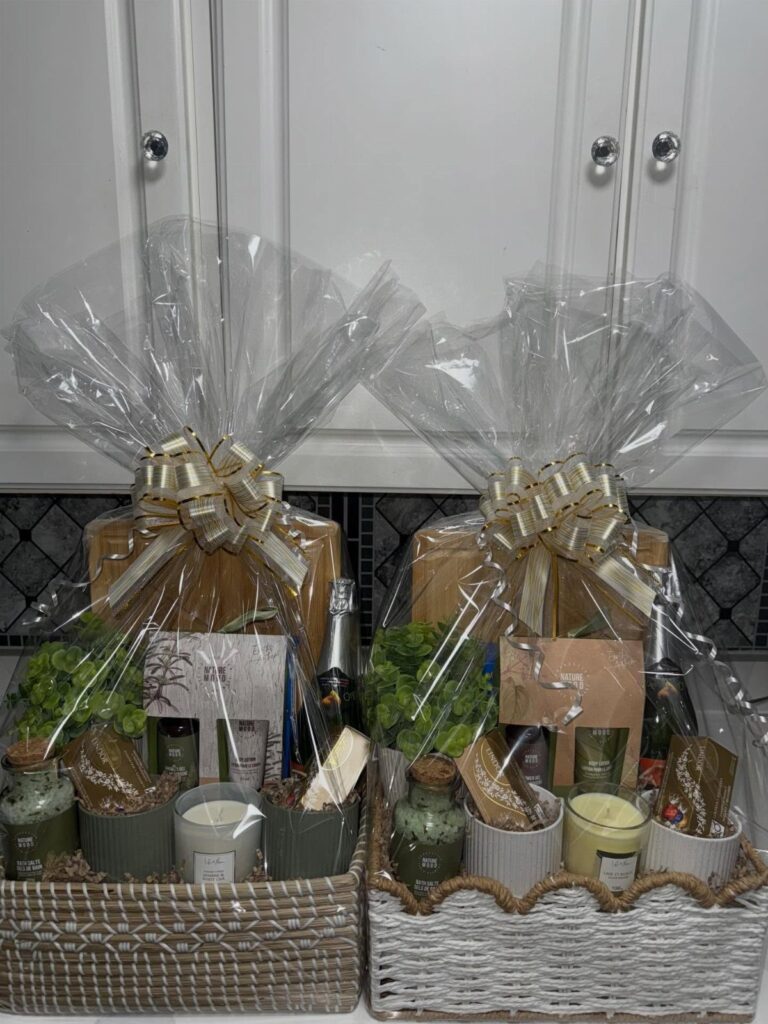 Two wrapped gift baskets containing wooden boards, candles, and plants in a kitchen.