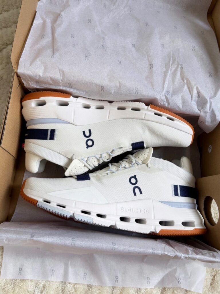 White On Cloud running shoes with navy accents inside a cardboard shoebox.