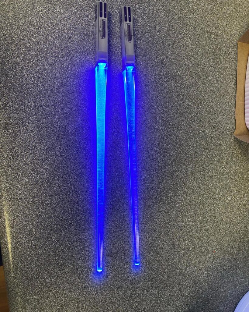 Glowing blue lightsaber chopsticks resting on a grey speckled surface.